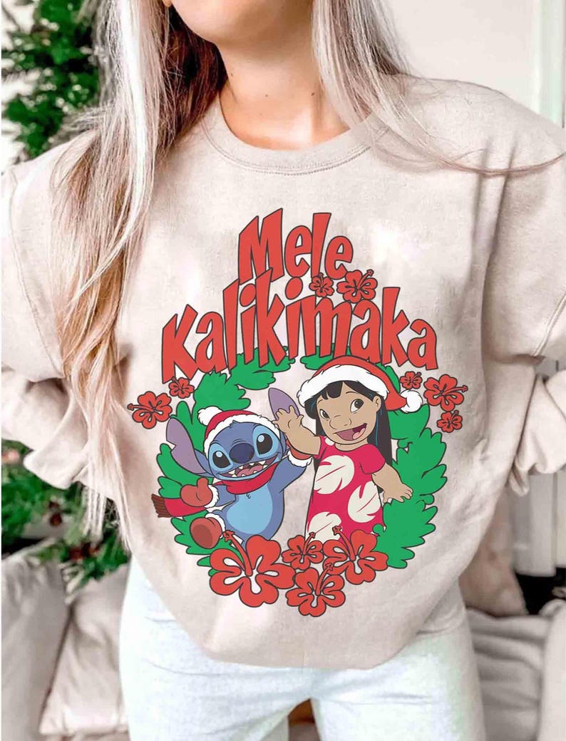 May include: Beige sweatshirt featuring the phrase "Mele Kalikimaka" in red script. The graphic includes cartoon characters Stitch and Lilo, surrounded by red flowers and green leaves, all wearing Santa hats. A festive holiday design.