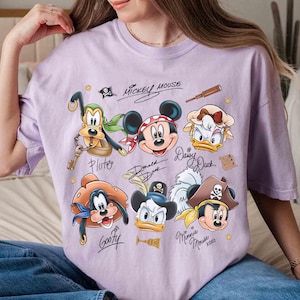 May include: A light purple t-shirt featuring a graphic of Mickey Mouse and friends in pirate attire. The design includes Pluto, Mickey, Daisy, Goofy, Donald, and Minnie Mouse, with their signatures. The words "Mickey Mouse" are also printed.