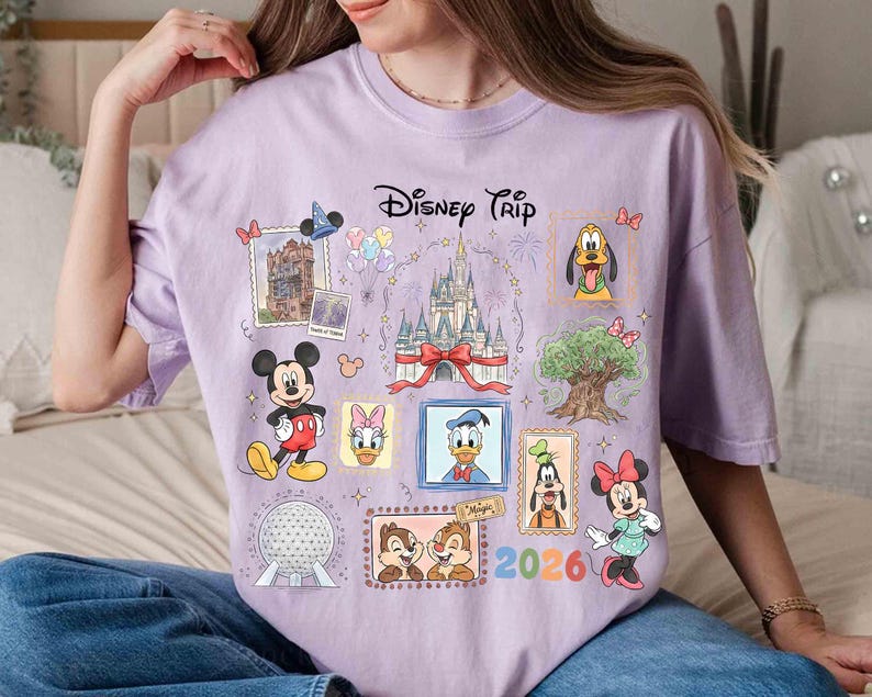 Puede incluir: Camiseta lila claro con un dise&ntilde;o de "Disney Trip". El gr&aacute;fico incluye ilustraciones de Mickey Mouse, Minnie Mouse, Donald Duck, Pluto y Chip y Chop, junto con un castillo y el a&ntilde;o 2026.