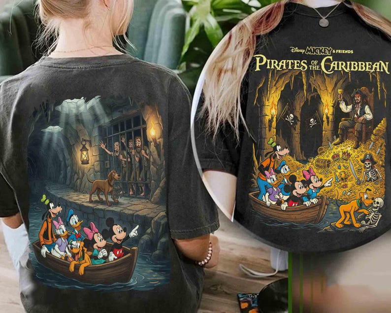 May include: Dark gray t-shirt featuring a colorful graphic of Disney characters in a boat, with a pirate-themed design. The back of the shirt shows a scene with a dog and prisoners behind bars. The text "Disney Mickey & Friends Pirates of the Caribbean" is printed on the shirt.