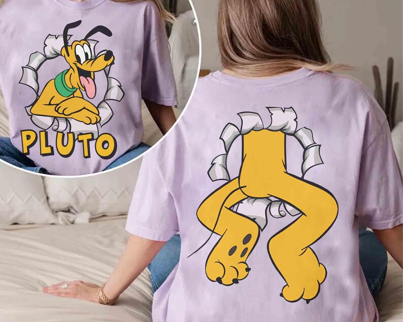 May include: A lilac t-shirt with a cartoon image of Pluto, the Disney dog, breaking through a paper design. The word "PLUTO" is printed in yellow. The back of the shirt shows Pluto's legs and paws.