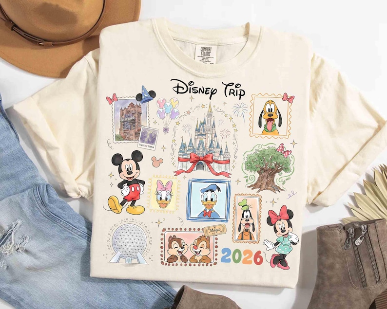 Puede incluir: Camiseta color crema con un dise&ntilde;o colorido de Disney Trip. El dise&ntilde;o incluye ilustraciones de Mickey Mouse, Minnie Mouse, el Pato Donald, Pluto, Chip y Chop, y el castillo de Cenicienta. El a&ntilde;o 2026 tambi&eacute;n est&aacute; impreso en la camiseta.