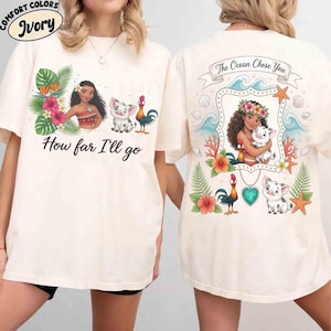 Op de afbeelding: Ivoor kleurig t-shirt met een afbeelding van een cartoonvrouw, een varken en een haan met de tekst "How far I'll go". De achterkant toont de vrouw met een varken en de tekst "The Ocean Chose You."