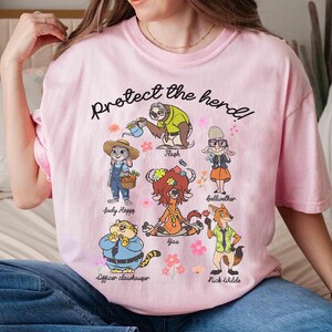 Peut inclure: T-shirt rose avec un graphique de personnages du film Zootopia. Le texte "Protect the herd!" est imprim&eacute; sur le t-shirt. Les personnages incluent Judy Hopps, Nick Wilde, Flash, Bellwether, Yax et Officer Clawhauser.