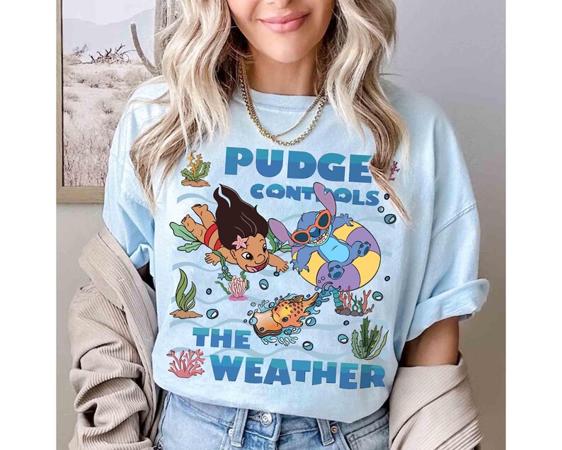 May include: Light blue t-shirt featuring a graphic of Lilo and Stitch in an underwater scene. The text "Pudge Controls The Weather" is displayed in blue. The design includes cartoon characters, coral, and seaweed.