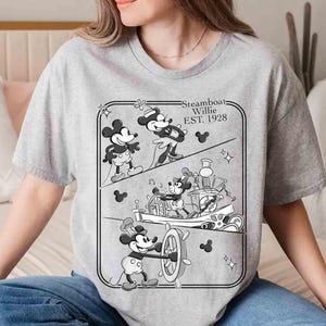 Może przedstawiać: Szara koszulka z czarno-białą grafiką Myszki Miki z filmu Steamboat Willie. Projekt przedstawia Myszkę Miki za sterem parowca i napis "Steamboat Willie EST. 1928".