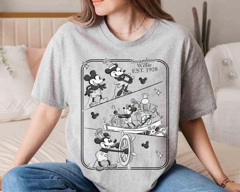 Może przedstawiać: Szara koszulka z czarno-białą grafiką Myszki Miki z filmu Steamboat Willie. Projekt przedstawia Myszkę Miki za sterem parowca i napis "Steamboat Willie EST. 1928".