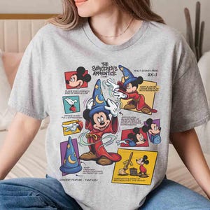May include: A gray t-shirt featuring a graphic of Mickey Mouse as the Sorcerer's Apprentice from Fantasia. The design includes text and illustrations detailing the character's features and the film's title.