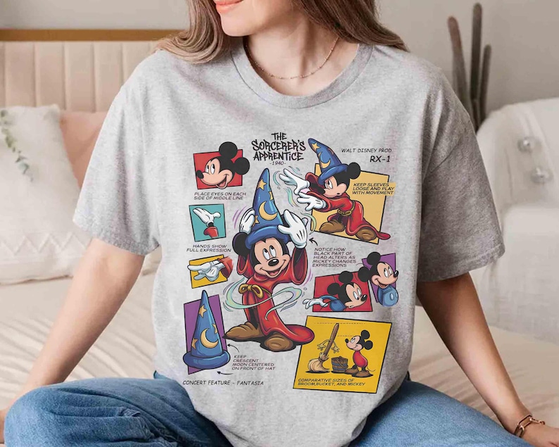 May include: A gray t-shirt featuring a graphic of Mickey Mouse as the Sorcerer's Apprentice from Fantasia. The design includes text and illustrations detailing the character's features and the film's title.