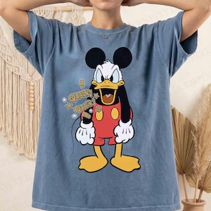 May include: A blue t-shirt with a cartoon character combining Mickey Mouse and a duck, wearing red shorts and holding a microphone. The shirt features the text "QUACK!" with star graphics.