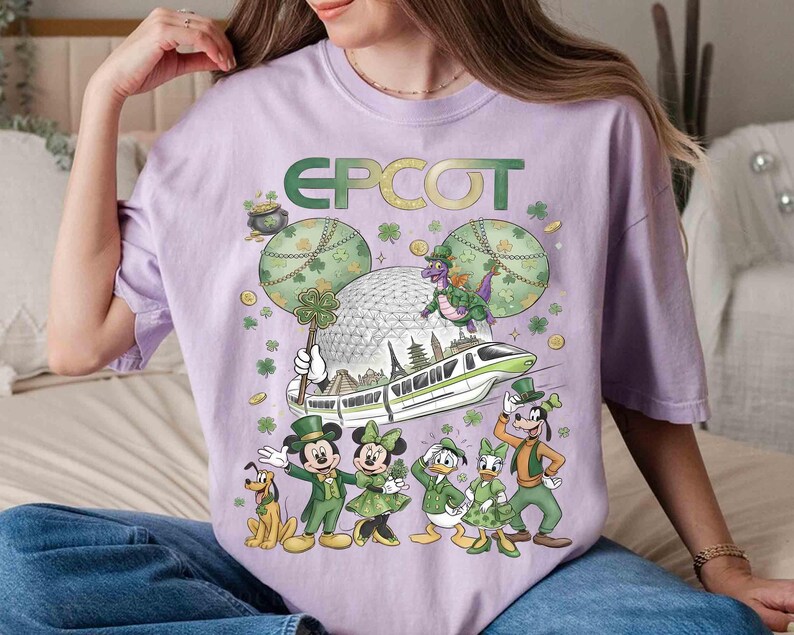 May include: A lilac t-shirt with the word "EPCOT" in green and gold. The design features Mickey and friends in green St. Patrick's Day outfits, a dragon, and the EPCOT sphere. The shirt has a loose fit.
