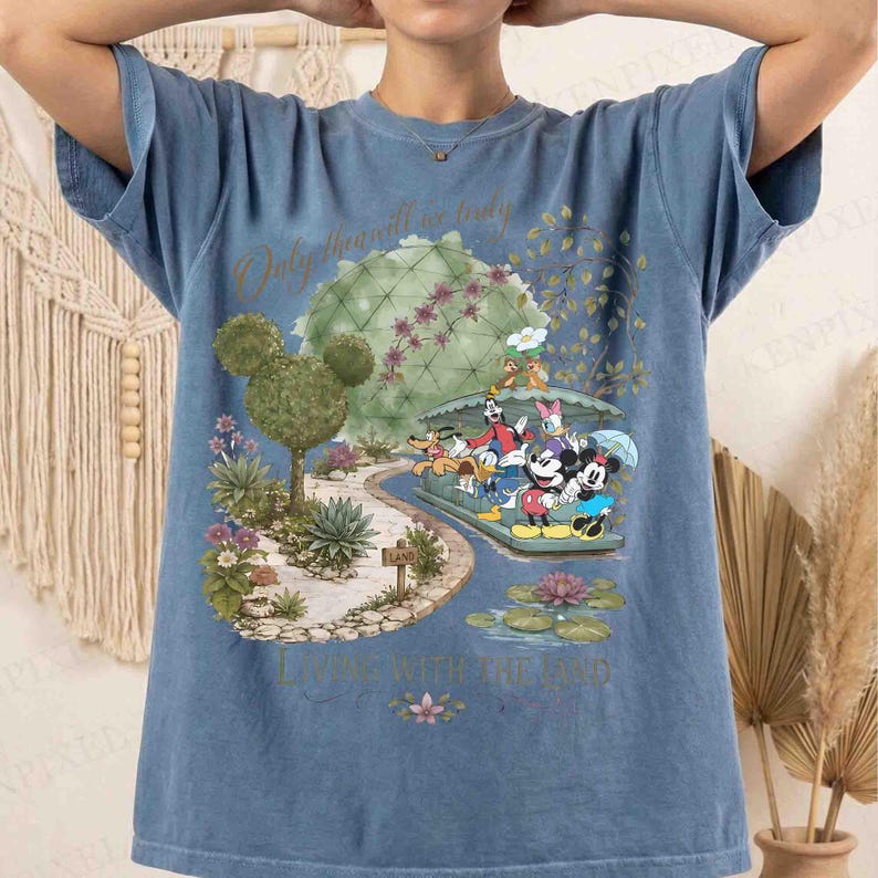 May include: Blue t-shirt featuring a colorful graphic of Disney characters, including Mickey and Minnie Mouse, in a whimsical garden setting. The shirt has the text "Only the will is truly living with the god".