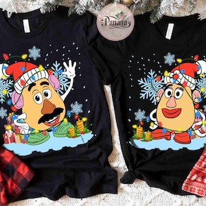 Könnte beinhalten: Schwarze T-Shirts mit weihnachtlichen Motiven von Mr. und Mrs. Potato Head. Jedes Shirt zeigt einen Cartoon-Kartoffelkopf mit Weihnachtsmütze, umgeben von Schneeflocken und Lichterketten. Das Design beinhaltet auch Geschenke und Kerzen.