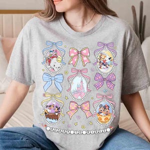 May include: A gray t-shirt with a graphic print of Disney characters in oval frames with pink bows and pastel colors. The text "Original to Timeless" is printed on the bottom of the shirt.