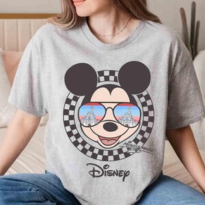May include: A gray t-shirt with a Mickey Mouse graphic. Mickey is wearing sunglasses with the Cinderella Castle reflected in them. The shirt also has the text "Mickey Mouse" and "Disney" printed on it.