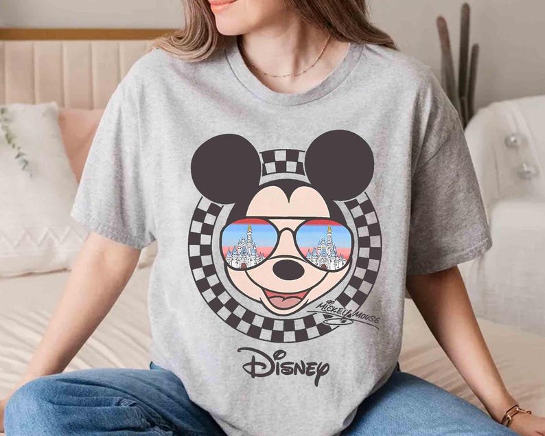 May include: A gray t-shirt with a Mickey Mouse graphic. Mickey is wearing sunglasses with the Cinderella Castle reflected in them. The shirt also has the text "Mickey Mouse" and "Disney" printed on it.