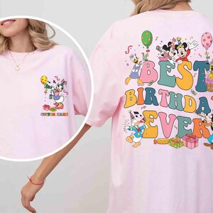 Pu&ograve; includere: T-shirt rosa chiaro con una grafica colorata di personaggi Disney che festeggiano un compleanno. Il testo "BEST BIRTHDAY EVER" &egrave; visualizzato sul retro. La parte anteriore ha una grafica pi&ugrave; piccola con il testo "CUSTOM NAME".