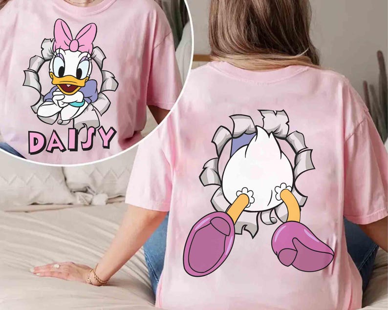 Puede incluir: Camiseta rosa claro con un dise&ntilde;o de Daisy Duck. La parte delantera de la camiseta muestra a Daisy rompiendo un efecto de papel rasgado, con su nombre debajo. La parte trasera de la camiseta muestra el trasero y los pies de Daisy saliendo del mismo efecto.