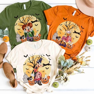 Peut inclure: Trois t-shirts sur le th&egrave;me d'Halloween en vert olive, orange et cr&egrave;me. Chaque chemise pr&eacute;sente un personnage de dessin anim&eacute; devant une pleine lune avec un arbre effrayant, des chauves-souris et des citrouilles. Les chemises sont pr&eacute;sent&eacute;es avec des chaussures et des citrouilles d&eacute;coratives.