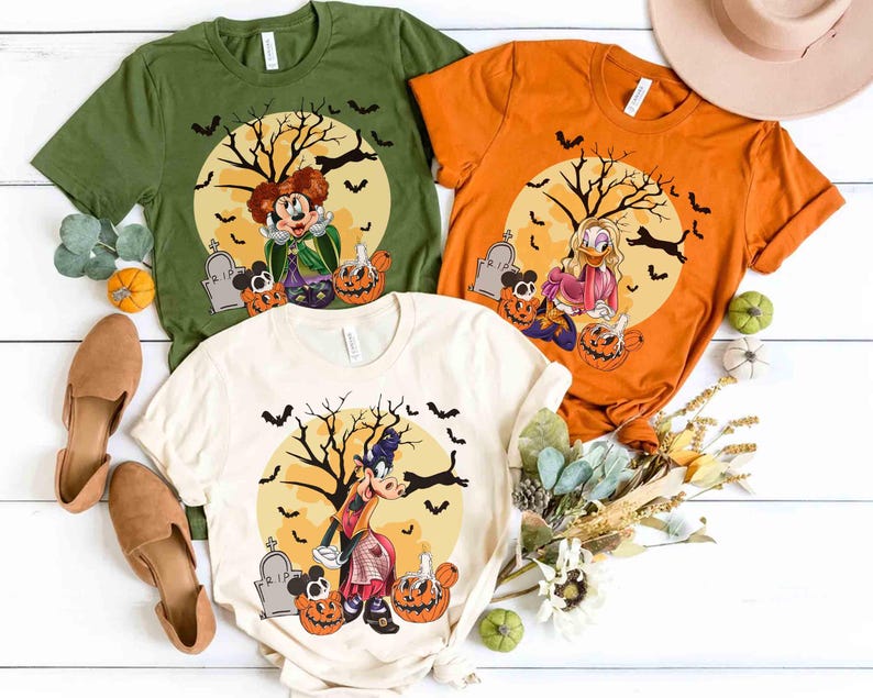 Peut inclure: Trois t-shirts sur le th&egrave;me d'Halloween en vert olive, orange et cr&egrave;me. Chaque chemise pr&eacute;sente un personnage de dessin anim&eacute; devant une pleine lune avec un arbre effrayant, des chauves-souris et des citrouilles. Les chemises sont pr&eacute;sent&eacute;es avec des chaussures et des citrouilles d&eacute;coratives.