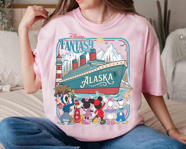 May include: Pink t-shirt featuring a Disney Fantasy Alaska cruise design. The graphic includes a cruise ship, cartoon characters, mountains, and the text "Disney Fantasy Alaska".