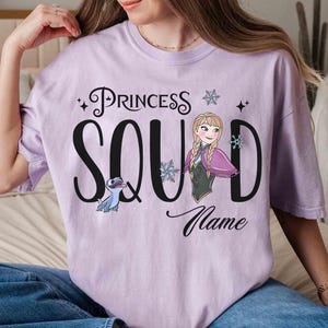 May include: A light purple t-shirt with the words "Princess Squad" in black script and a cartoon image of Anna from Frozen. The shirt also features a cartoon image of a blue creature and snowflakes.