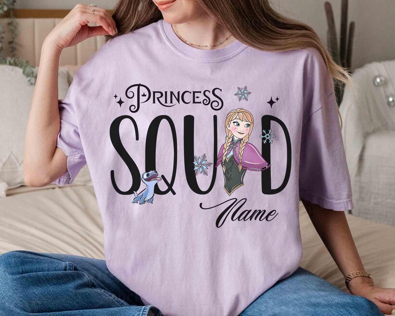 May include: A light purple t-shirt with the words "Princess Squad" in black script and a cartoon image of Anna from Frozen. The shirt also features a cartoon image of a blue creature and snowflakes.