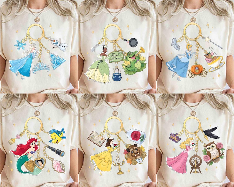 May include: Cream-colored t-shirts featuring various Disney princess-themed keychains. Each keychain showcases a different princess with related icons, such as a mermaid, a glass slipper, and a rose. The designs are colorful and whimsical.
