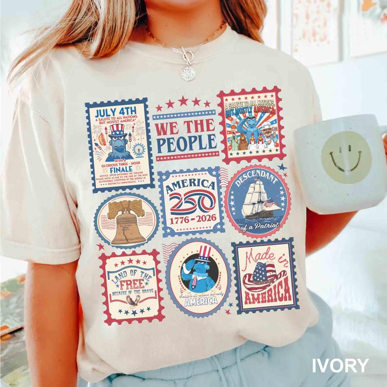 以下が含まれることがあります： アイボリー色のTシャツ。愛国的な切手のデザインのコラージュが特徴です。切手には、自由の鐘、船、そして「7月4日」と「アメリカ」の文字が描かれています。Tシャツには「We the People」の文字も入っています。
