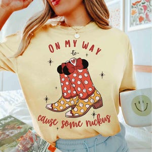 Peut inclure: T-shirt jaune avec un motif de bottes &agrave; pois rouges et blancs avec un n&oelig;ud et le texte "On my way -to- cause some ruckus".