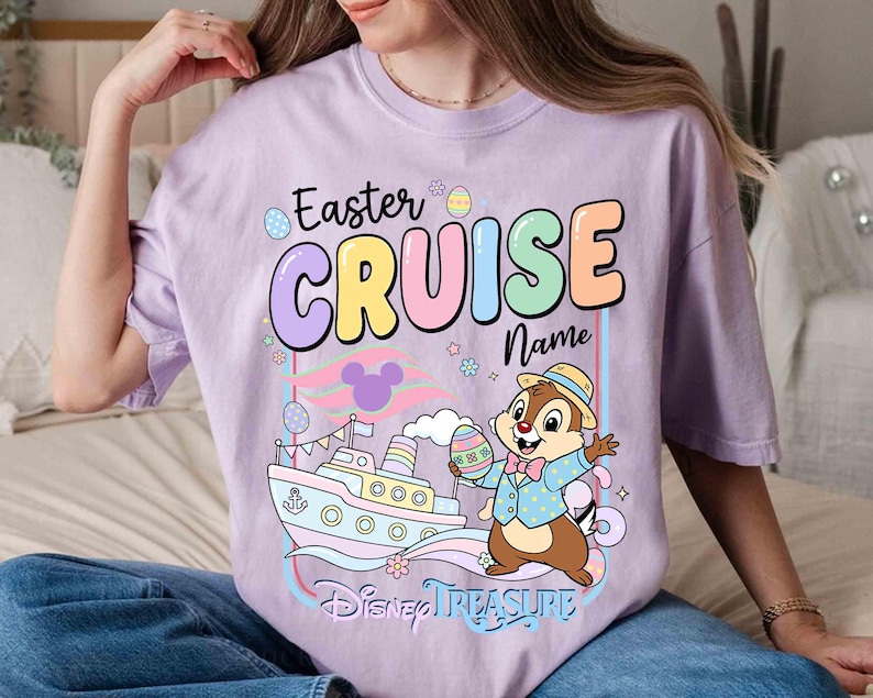 K&ouml;nnte beinhalten: Helllila T-Shirt mit der Aufschrift "Easter CRUISE Name" in Pastellfarben. Eine Zeichentrickfigur h&auml;lt ein Osterei in der N&auml;he eines Schiffs, darunter steht "Disney TREASURE".