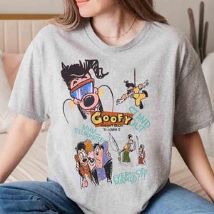 May include: Grey t-shirt featuring a cartoon graphic of Goofy and other Disney characters. The text on the shirt reads "Goofy Doesn't Begin To Cover It" and "Stand Out".