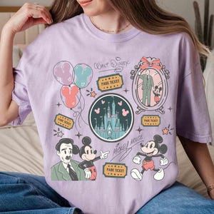 Peut inclure: Un t-shirt lilas avec un motif de dessin anim&eacute; repr&eacute;sentant Mickey Mouse, Walt Disney et un ch&acirc;teau. Le t-shirt comprend des illustrations de ballons, de billets de parc et d'&eacute;toiles. Les mots "Walt Disney" et "Mickey Mouse" sont &eacute;galement imprim&eacute;s.