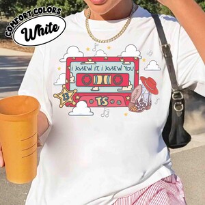 May include: A white t-shirt featuring a graphic print of a red cassette tape with the text 'I KNEW IT, I KNEW YOU' and 'TS'. The design includes a yellow sheriff star with the number 13, a cowboy boot, clouds, stars, and musical notes.