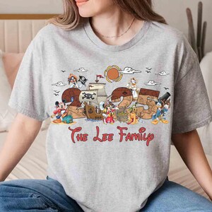 May include: A grey t-shirt with a pirate-themed design, the number "25", and cartoon characters. The text "The Lee Family" is written in red script below the design. The shirt has short sleeves.