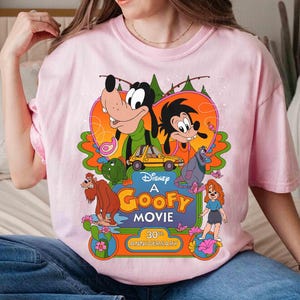 May include: Pink t-shirt with a graphic of Goofy and other Disney characters from the movie "A Goofy Movie". The graphic includes the text "Disney's A Goofy Movie 30th Anniversary".