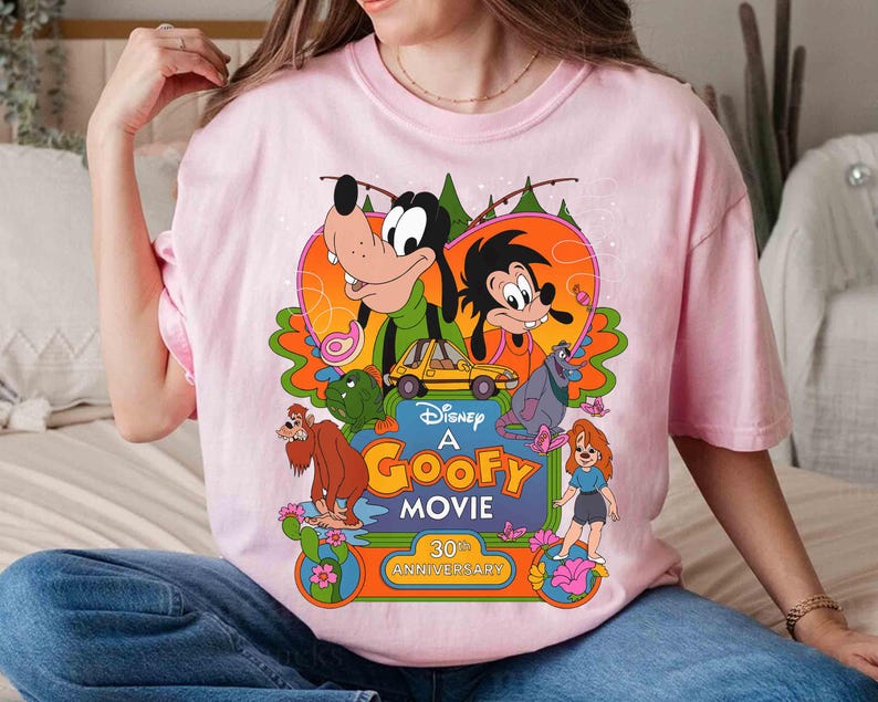 May include: Pink t-shirt with a graphic of Goofy and other Disney characters from the movie "A Goofy Movie". The graphic includes the text "Disney's A Goofy Movie 30th Anniversary".