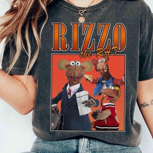 May include: A dark grey t-shirt with a vintage-style graphic of three cartoon rats. The graphic features the text "Rizzo the Rat" in orange and white lettering.