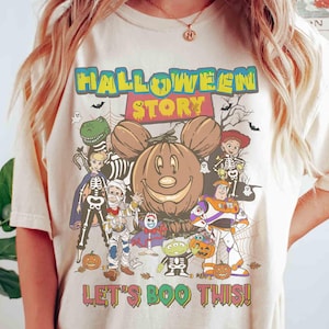 Puede incluir: Camiseta color crema con un dise&ntilde;o tem&aacute;tico de Halloween. El dise&ntilde;o incluye una calabaza sonriente con orejas de Mickey Mouse, varios personajes de dibujos animados con disfraces de Halloween y el texto "HALLOWEEN STORY" y "LET'S BOO THIS!"