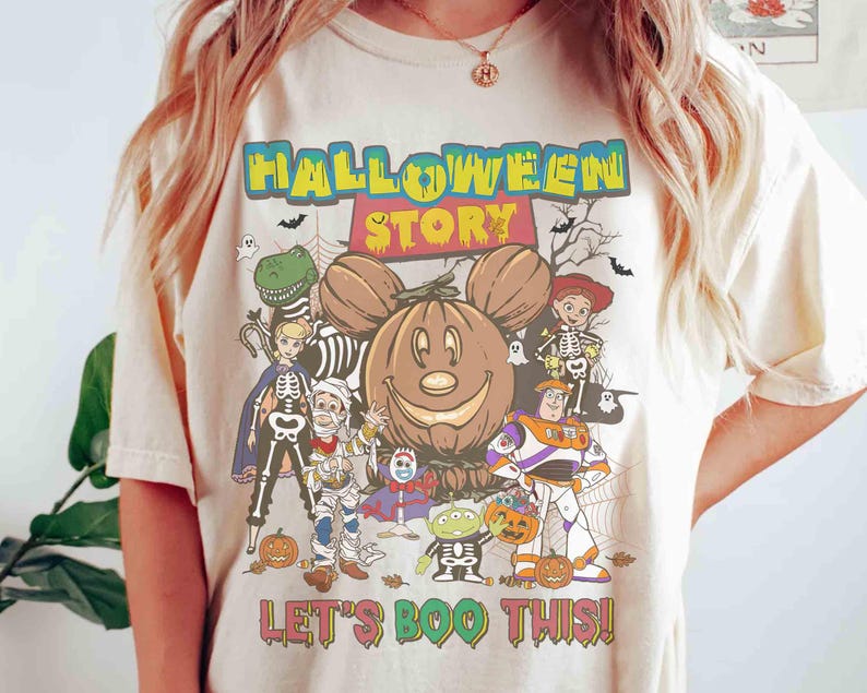 Puede incluir: Camiseta color crema con un dise&ntilde;o tem&aacute;tico de Halloween. El dise&ntilde;o incluye una calabaza sonriente con orejas de Mickey Mouse, varios personajes de dibujos animados con disfraces de Halloween y el texto "HALLOWEEN STORY" y "LET'S BOO THIS!"