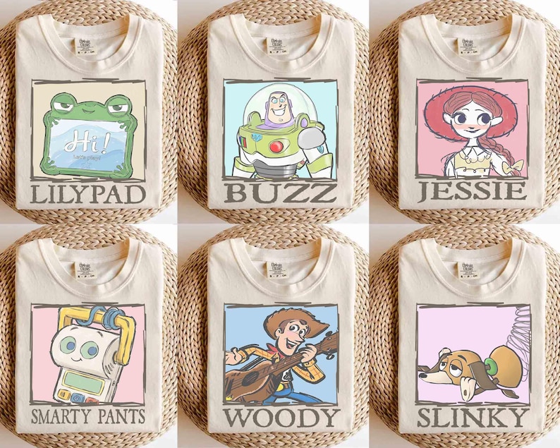 May include: Six cream-colored t-shirts, each featuring a different cartoon character design. The designs include a frog, Buzz Lightyear, Jessie, Smarty Pants, Woody, and Slinky. Each design is framed with a colored border and character name.