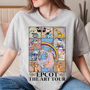 May include: A gray t-shirt featuring a colorful graphic of Disney characters in a grid, including Mickey Mouse, Minnie Mouse, and Donald Duck. The graphic includes a rainbow and the text "EPCOT THE ART TOUR".