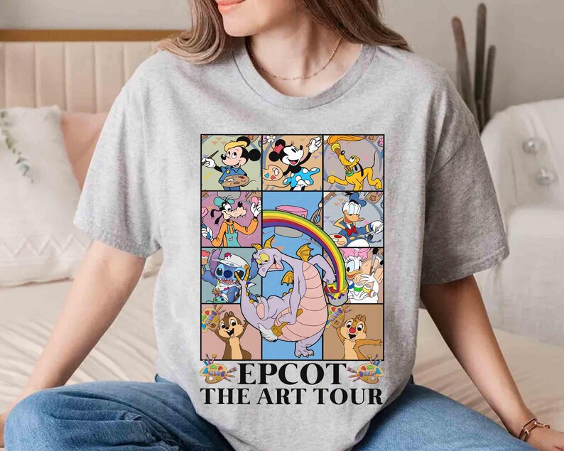 May include: A gray t-shirt featuring a colorful graphic of Disney characters in a grid, including Mickey Mouse, Minnie Mouse, and Donald Duck. The graphic includes a rainbow and the text "EPCOT THE ART TOUR".