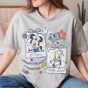 May include: A gray t-shirt featuring two framed cartoon images. One shows Minnie Mouse in a sailor outfit, the other shows Daisy Duck in a sailor outfit. The shirt has the words "Best Friends Forever" and other graphics.