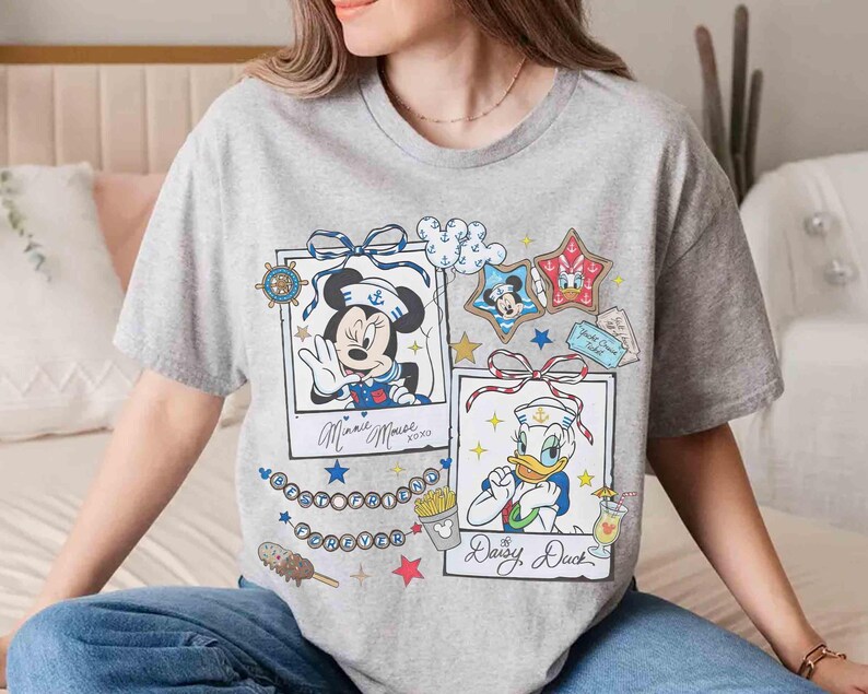 May include: A gray t-shirt featuring two framed cartoon images. One shows Minnie Mouse in a sailor outfit, the other shows Daisy Duck in a sailor outfit. The shirt has the words "Best Friends Forever" and other graphics.