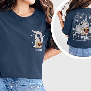 May include: Navy blue t-shirt with a Disneyland Halloween design. The front has a stylized "D" with a ghost and pumpkin. The back shows a castle, ghost, and pumpkins with the text "Disneyland est. 1955."
