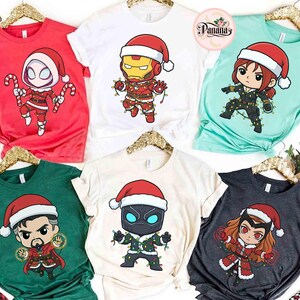 May include: A collection of Christmas-themed t-shirts featuring various Marvel characters in Santa hats and festive attire. The shirts are in red, white, green, and teal, with character designs including Spider-Man, Iron Man, Black Widow, Doctor Strange, Black Panther, and Scarlet Witch.