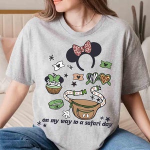 K&ouml;nnte beinhalten: Graues T-Shirt mit einem grafischen Design mit einem Minnie-Mouse-Ohren-Haarreif, einer Bauchtasche und anderen Safari-Elementen. Der Text "on my way to a safari day" ist auf dem Shirt aufgedruckt.