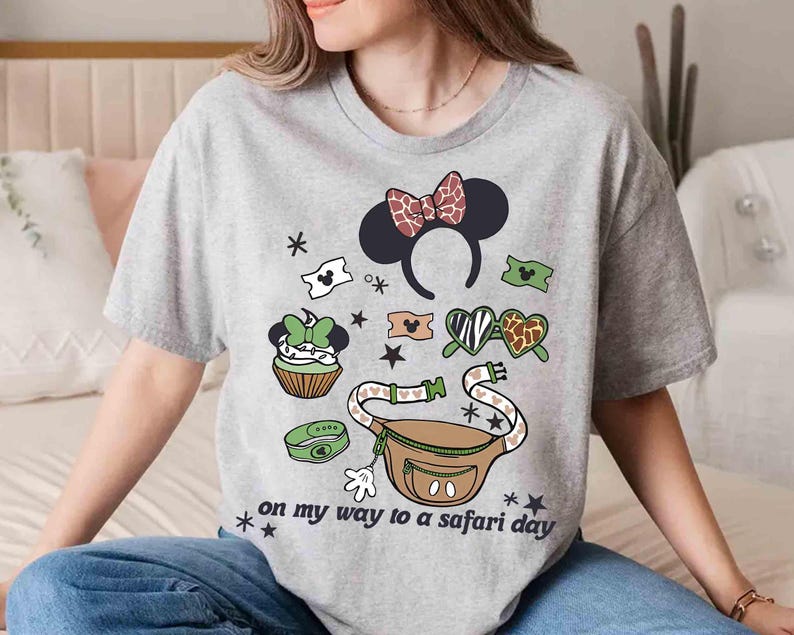 K&ouml;nnte beinhalten: Graues T-Shirt mit einem grafischen Design mit einem Minnie-Mouse-Ohren-Haarreif, einer Bauchtasche und anderen Safari-Elementen. Der Text "on my way to a safari day" ist auf dem Shirt aufgedruckt.