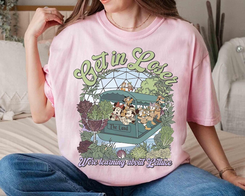 May include: Pink t-shirt with a graphic featuring Disney characters on a boat ride with the text "Get in Lose" and "We're learning about Lettuce". The design includes green and purple botanical elements.